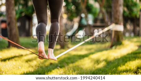 Slacklining is a practice in balance that typically uses nylon or polyester webbing. Girl walking on a slackline in a park during a sunset. Slack line