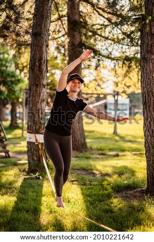 Slacklining is a practice in balance that typically uses nylon or polyester webbing. Girl walking on a slackline in a park during a sunset. Slack line