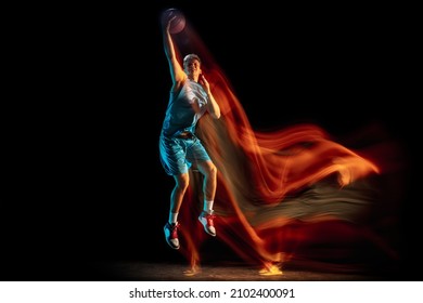 Slam dunk. Young caucasian male basketball player playing basketball isolated over dark studio background in mixed light. Concept of motion, power, speed, healthy lifestyle, professional sport.