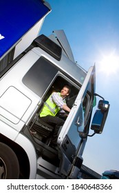 A Slanted Low Angle Vertical Shot Of A Truck Driver In Safety Vest Sitting Inside The Cab Of A Semi-truck On A Bright Sunny Day While Closing The Door.