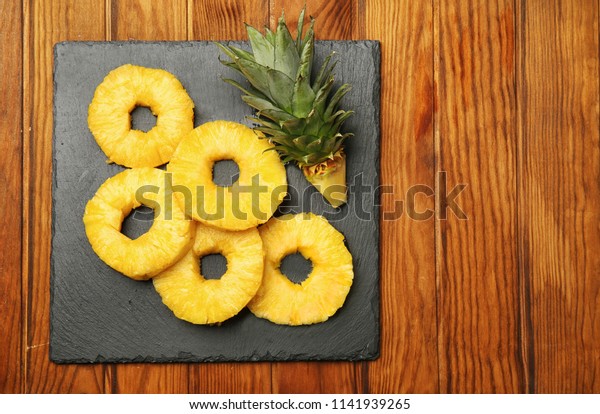 Slate plate with canned pineapple rings on\
wooden background