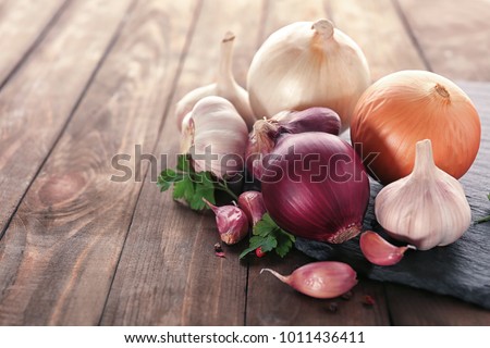 Slate plate with fresh garlic and onion on wooden table, closeup