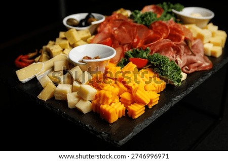 Slate platter filled with various types of cheese, salami, ham, and olives for a gathering.