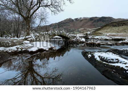 Slaters Bridge in Little Langdale on a cold Winters morning with snow on rocks. Lake District, UK.