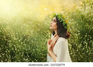 slavic fantasy young woman praying, hands folded in prayer pose. White traditional dress, herbal wreath on head. Nature summer, green grass, divine magic light, bright sun. Girl holiday Ivan Kupala