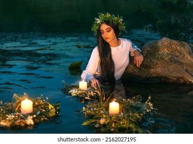 Slavic woman nymph stands in water herbal wreath floa candles burning. Fantasy girl mermaid. White long wet dress. Summer night green grass tree river. pagan holiday Ivan Kupala divination maidens. - Shutterstock ID 2162027195
