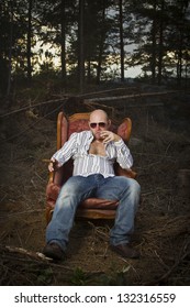 Sleazy Man In A Classic Vintage Chair In The Middle Of A Logging Area. Smoking Cigar And Drinking Cognac In Woods.