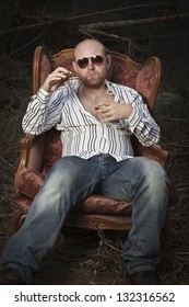 Sleazy Man In A Classic Vintage Chair In The Middle Of A Logging Area. Smoking Cigar And Drinking Cognac In Woods.
