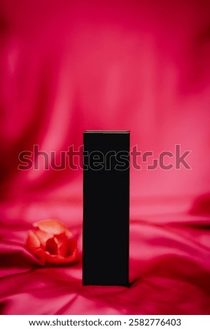 A sleek black rectangular object on vibrant pink satin fabric, with a soft-focus orange flower in the background, creating a stylish composition.