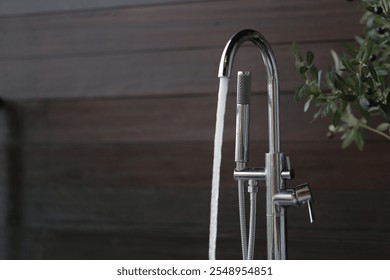 A sleek chrome bathtub faucet with running water, set against a backdrop of marble tiles and an elegant bathroom decor. This modern fixture adds a touch of luxury and style to any bathroom. - Powered by Shutterstock