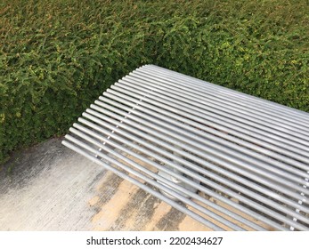 Sleek Design Silver Metal Bench At Public Park Surrounded By Green Shurbs.