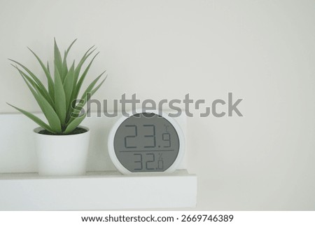 A sleek digital clock displays temperature and humidity beside a small plant