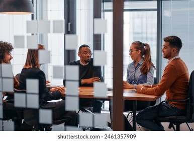 In a sleek glass office space, a team of business professionals engage in lively discussions and exchange strategic ideas, showcasing collaboration and innovation at the heart of modern corporate - Powered by Shutterstock