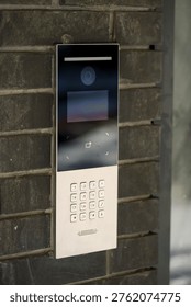 A sleek intercom system with a digital display and keypad is mounted on a textured brick wall, designed for secure entry access control