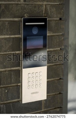 A sleek intercom system with a digital display and keypad is mounted on a textured brick wall, designed for secure entry access control