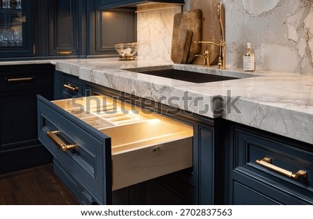 A sleek kitchen interior featuring a marble countertop and dark blue cabinets with golden handles and a drawer open.