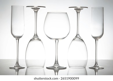 A sleek lineup of five elegant, empty wine glasses with long stems, reflecting on a glossy surface against a soft gray background, perfect for dining or event themes.