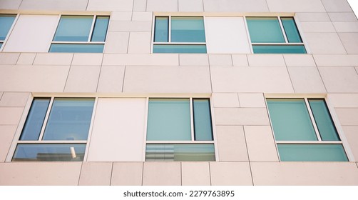 A sleek and modern building exterior with clean lines and large windows that reflect the blue sky. The building features a mix of concrete, steel, and glass, a futuristic and sophisticated look  - Shutterstock ID 2279763895