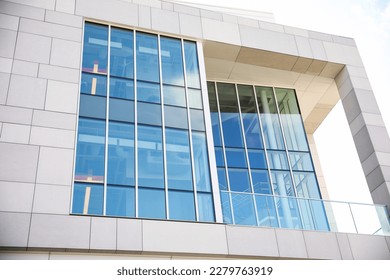 A sleek and modern building exterior with clean lines and large windows that reflect the blue sky. The building features a mix of concrete, steel, and glass, a futuristic and sophisticated look  - Shutterstock ID 2279763919