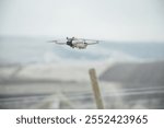 A sleek, modern drone captured in flight, showcasing its advanced technology against a soft, muted landscape.