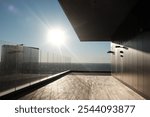 A sleek rooftop terrace bathed in sunlight, featuring a glass railing and modern architecture, offering a panoramic city view under a bright blue sky.