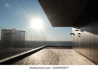 A sleek rooftop terrace bathed in sunlight, featuring a glass railing and modern architecture, offering a panoramic city view under a bright blue sky. - Powered by Shutterstock