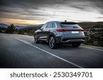 A sleek SUV driving on a curvy mountain road during sunset, with the vehicle