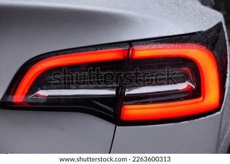 Sleek tail light of a silver fast car . Red lamp in parking position . The car is rainy and full of water drops . Car Detail View Close-Up Macro . Electrical Vehicle Tesla Car concept from behind .