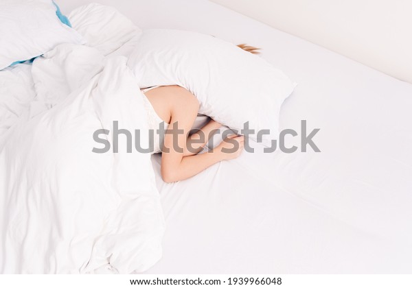 Sleep, early morning, waking up,\
noisy neighbors interfere, lack of sleep, too lazy to get out of\
bed. Young caucasian woman sleeps covering her head with\
pillows.