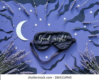 Sleep mask with lavender on dark blue color background with black clouds, Moon and stars. Text Good night on the mask. Quality of sleep, aromatherapy, herbal remedies. Creative flat lay.