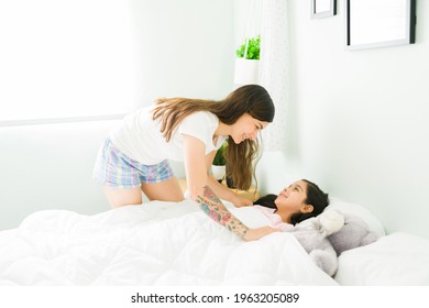 Sleep Tight, Kid. Cheerful Mom In Pajamas Tucking In Her Little Daughter In Bed And Smiling While Wishing A Goodnight 