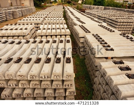 Sleepers stock in railway depot. Concrete railway ties stored for reconstruction of old railway station. Old houses and highway bridge in background