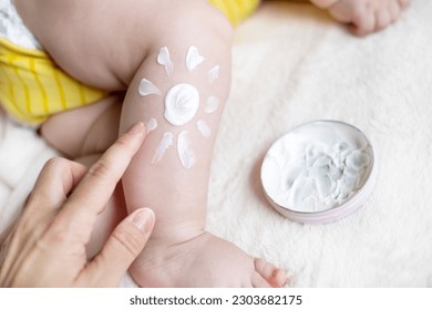 sleeping adorable baby boy on blanket with drawn sun painted from body lotion on leg.mother hand applying cream sun protection sunblock.vacation.fat toddler infant cute feet child in yellow bodysuit - Powered by Shutterstock
