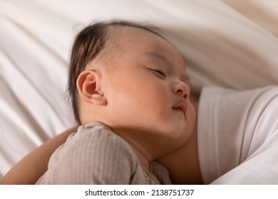 Sleeping Baby Boy Is Snuggling With Mom Is The Most Warmest Moment. An Innocent Asian Kid Is Chubby, Cute In Grey Pajamas Laying Down With Mom On White Sheet And Comfy Mattress In The Bedroom.