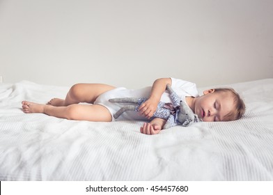 Sleeping baby in his crib, holding a teddy bear.