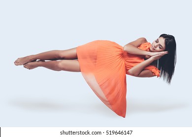 Sleeping Beauty. Full Length Studio Shot Of Attractive Young Woman In Orange Dress Hovering In Air And Keeping Eyes Closed