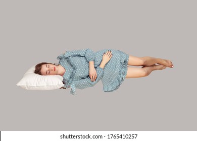 Sleeping Beauty Hovering In Air. Relaxed Girl In Vintage Ruffle Dress Lying Comfortably On Pillow Levitating, Keeping Eyes Closed, Watching Dreams. Full Length Studio Shot Isolated On Gray, Indoor