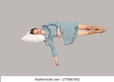 Sleeping Beauty Hovering In Air. Relaxed Girl In Vintage Ruffle Dress Lying Comfortably On Pillow Levitating, Keeping Eyes Closed, Watching Dreams. Full Length Studio Shot Isolated On Gray, Indoor