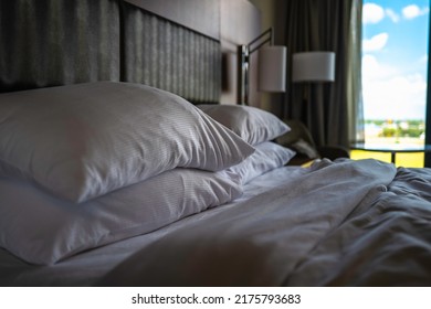 Sleeping Bed With Soft White Pillows And Light Lamps And A Blurred Window View. Travel Lodging Background Image.