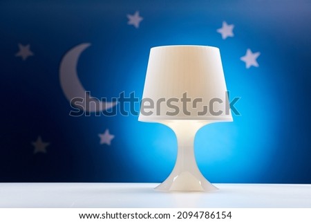 sleeping and bedtime concept - close up of night lamp on table over moon and stars on blue background
