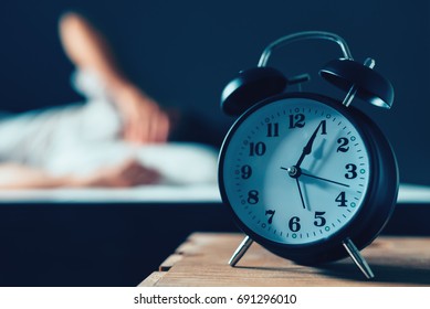 Sleeping Disorder Or Insomnia Concept, Selective Focus Of Vintage Clock In Bedroom And Out Of Focus Male Person Trying To Fall Asleep In Bed