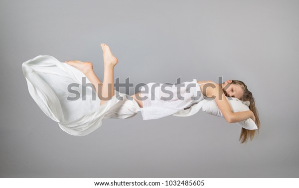寝てる女の子 夢の中で飛ぶ 空を飛ぶ白いリネン 明るいグレイの背景 の写真素材 今すぐ編集