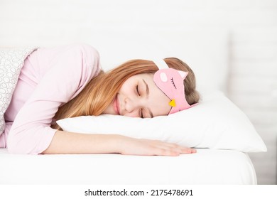 Sleeping Girl Wearing Funny  Eyemask Lying On A Pillow In Bedroom. Cute Teen Girl With Closed Eyes Smiling Having A Dream. Healthy Sleep, Sweet Dreams Concept. Copy Space. Selective Focus.