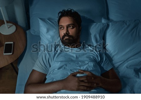 sleeping, insomnia and people concept - speelpess indian man lying in bed at home at night