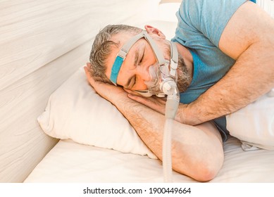 Sleeping man with chronic breathing issues considers using CPAP machine in bed. Healthcare, Obstructive sleep apnea therapy, CPAP, snoring concept - Shutterstock ID 1900449664