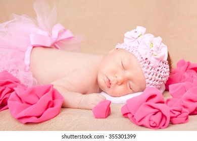 A sleeping newborn baby girl wearing a pink headband and tutu.