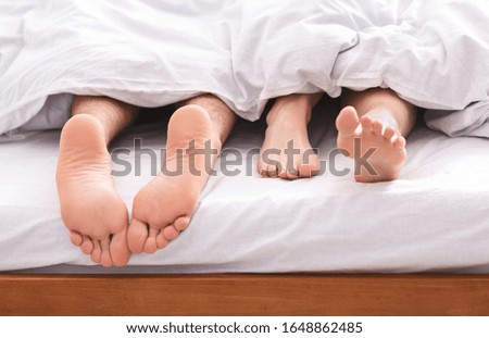 Sleeping styles. Married man and woman feet under white duvet in bed