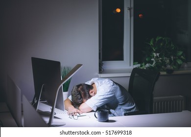 Sleeping Young Man Working On Computer At Night In Dark Office. The Designer Works In The Later Time. A Young Man Sits At The Computer