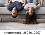 Sleeping young married couple lying upside down on home sofa, having fun, keeping strange funny pose for relaxation on comfortable couch, relaxing with head and hair hanging to floor