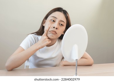 Sleepless Asian woman looking her face in the mirror and worry about dark circles under eyes - Shutterstock ID 2284002979